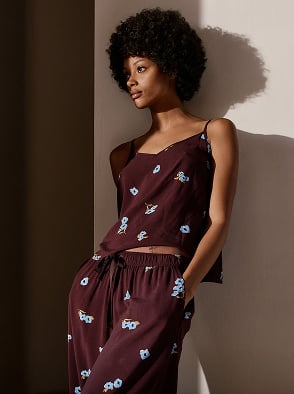 Woman in a white patterned dress standing outdoors in a sunlit street with a pink building in the background.